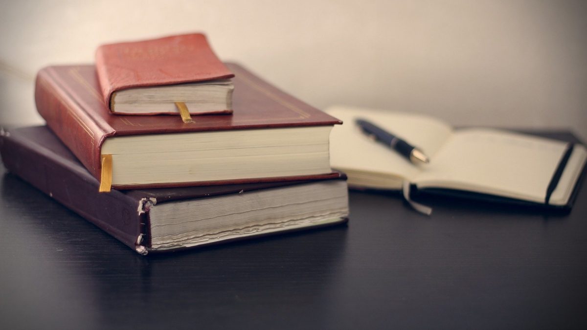 A stack of three books and an open notebook with a pen in it