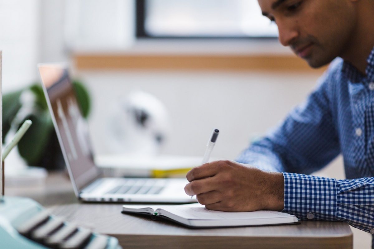 A person works at a desk with an open laptop and notebook