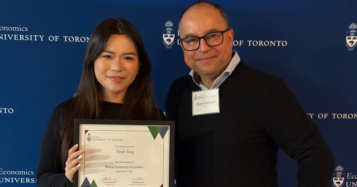 Standing in front of a UofT economics department banner are one award winning student and economics professor.